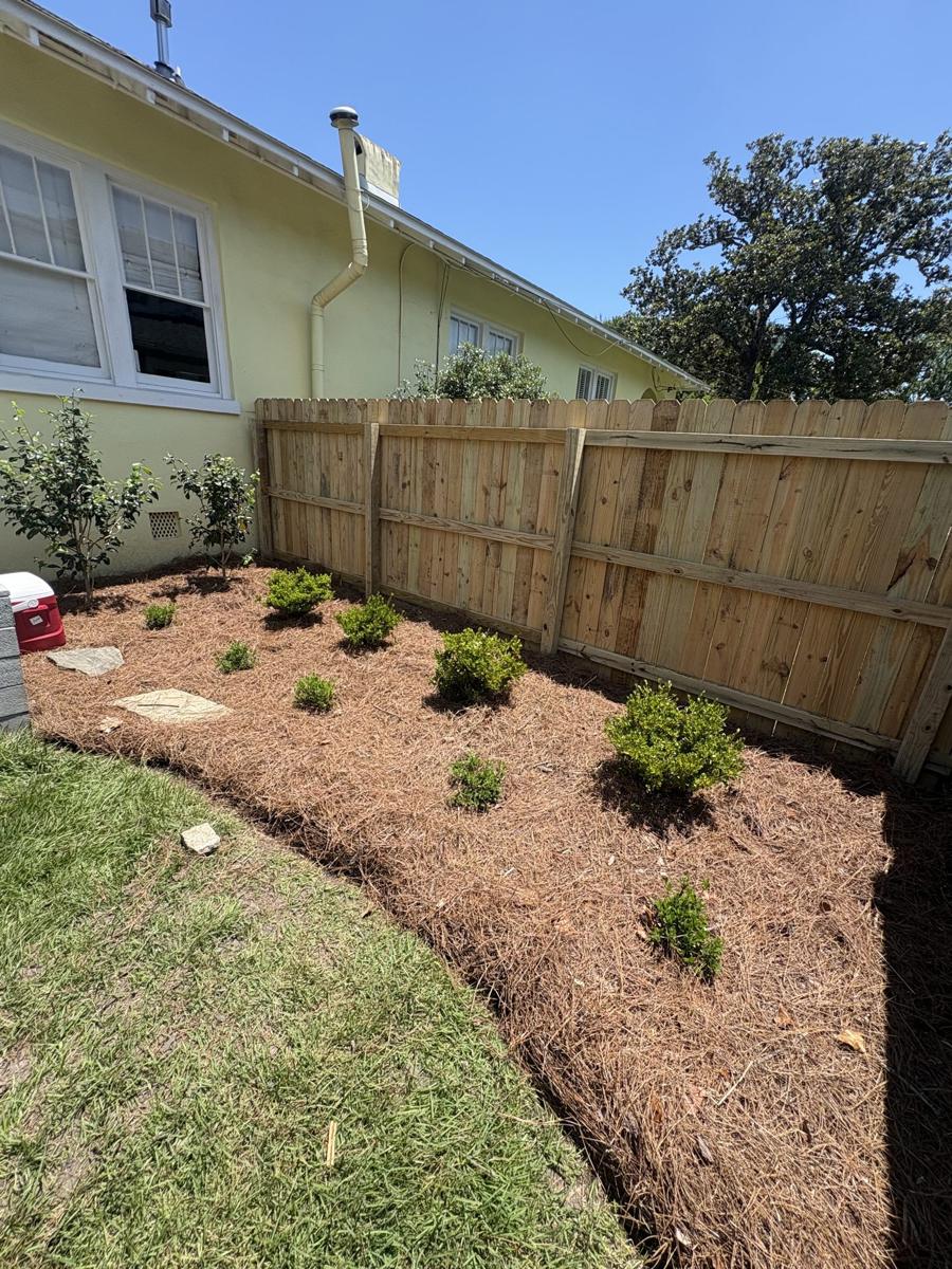 Backyard bed filled with fresh red mulch along a fence