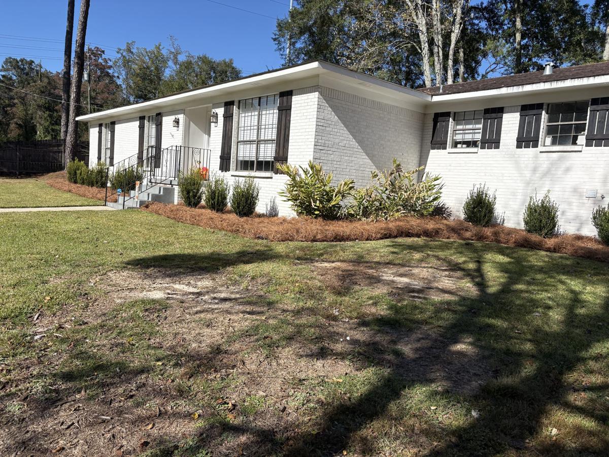 Pine straw beds along a white brick ranch house