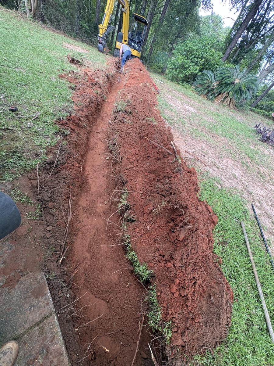 French drain trench cut through red clay along a lawn