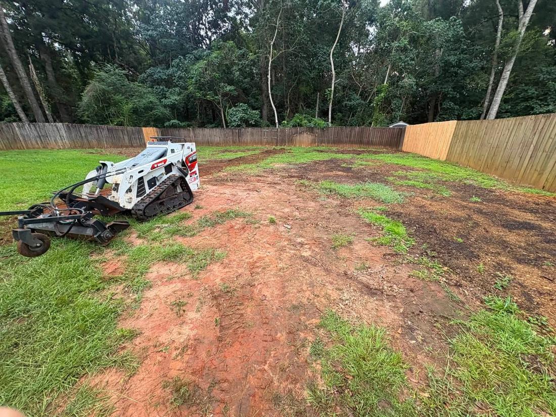 Skid steer with a Harley rake grading the same backyard